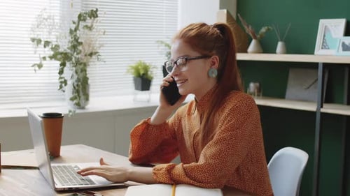 Woman Chatting on Phone While Working on Laptop