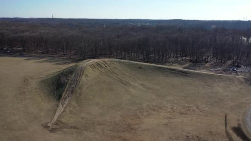 An aerial shot over an open field on a sunny day. The camera dolly & tilt down towards a ridge in th