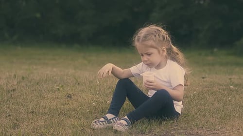 Little Girl Eating Snack on Grassy Lawn