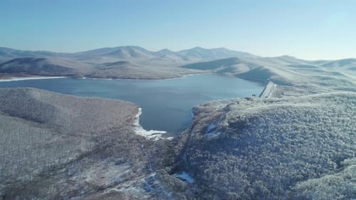 Aerial View on a Blue Lake Between the Snowy Mountains and Iced Frozen Forest