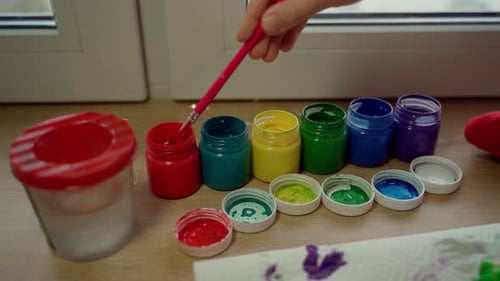 Child's Hand Dipping Paintbrush into Red Paint