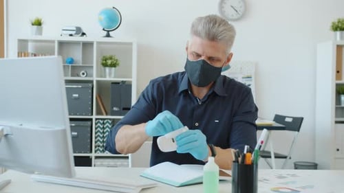 Office Worker Wet Wiping Computer with Hand Sanitizer at Work During Pandemic