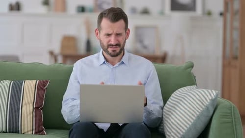 Young Man with Laptop Reacting To Failure on Sofa