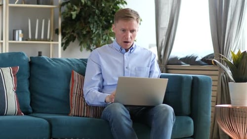 Man Uses Laptop in Living Room, Reacts in Surprise