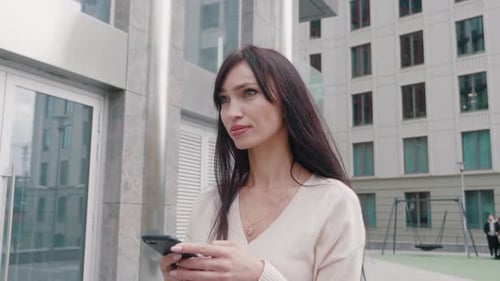 Young Beautiful Businesswoman Using Smartphone and Walking on City Streets of Downtown
