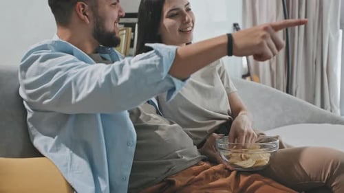 Young Couple Watching TV And Eating Chips At Home