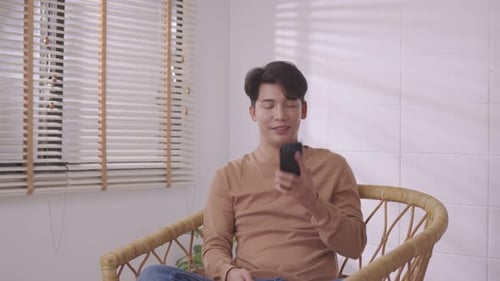 Em sua sala de estar, um homem asiático está ao telefone, ouvindo e conversando em seu smartphone.