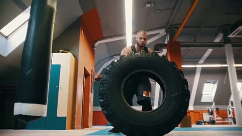 A Big Man Bodybuilder Turning Over the Tire on the Floor and Moving It