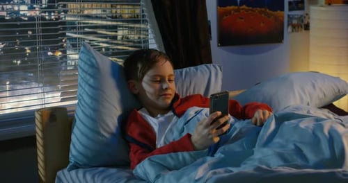 Boy Looking at Phone in Bed at Night