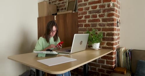 Woman Uses Phone and Laptop at Desk