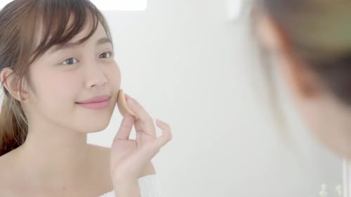 Young Woman Applying Foundation in Bathroom Mirror