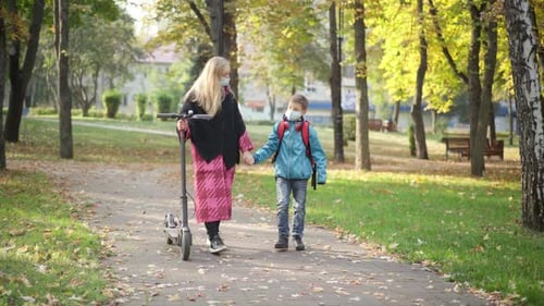 Wide Shot of Relaxed Caucasian Mother and Son in Coronavirus Face Masks Walking in Autumn Park with