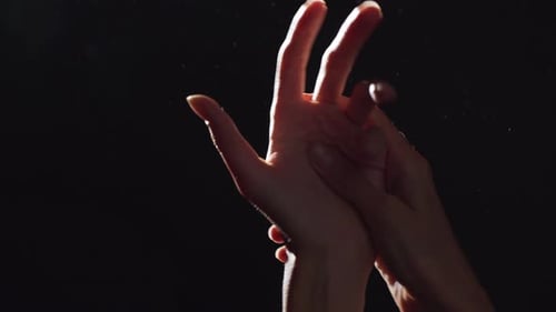 Silhouette Portrait of Two Caucasian Female Arms Closeup Rubbing Hands in Light with Flying Dust