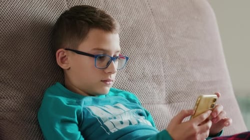 Young Boy Relaxing on Couch Using Mobile Phone