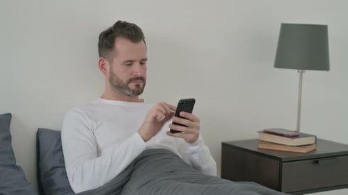 Man Using Phone While Lying in Bed