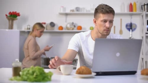 Couple in Kitchen, Man Works on Laptop
