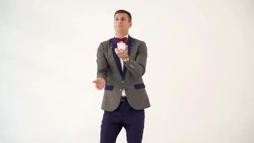 Homem em um terno cinza e azul está fazendo malabarismos como um palhaço no estúdio.