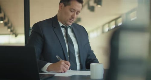 Businessman in Suit Writing on Paper at Desk