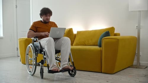 Man in Wheelchair Uses Laptop in Modern Apartment