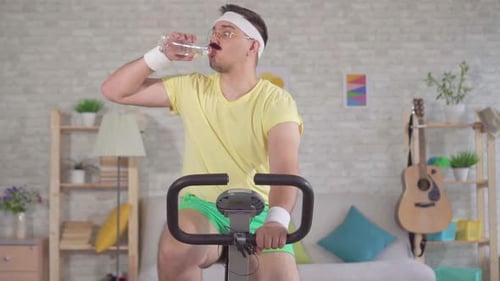 Man Drinks Water on Stationary Bike in Apartment
