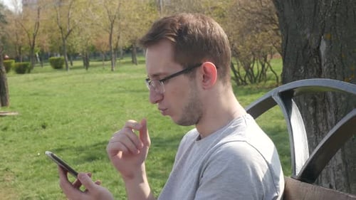 Man In A Park In The Summer Uses A Smartphone