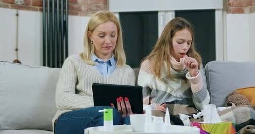 Mulher sentada com a filha no sofá macio e programas de revisão no tablet