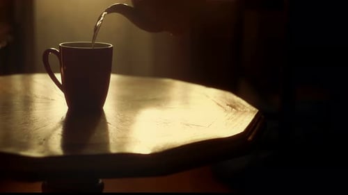 The Teapot Pours Hot Tea Into a Cup in the Golden Rays of the Sun