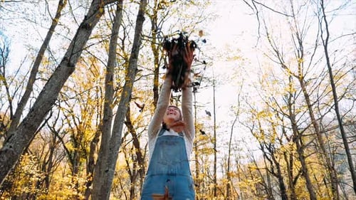 Happy Young Woman Having Fun and Throwing Yellow Leaves at Autumn Forest