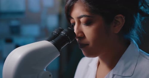 Woman Examining Sample Through Microscope in Lab