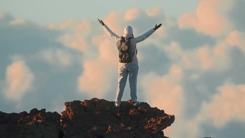 Woman with Backpack on Top of Cinematic Mountain Summit Above Clouds Sunset