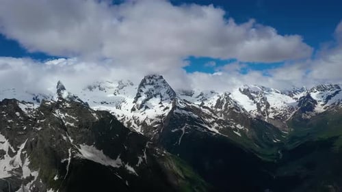 Air Flight Through Mountain Clouds Over Beautiful Snowcapped Peaks of Mountains and Glaciers