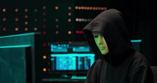 Hooded Hacker Typing at Computer in Dark Room