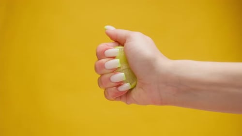 Hand Squeezing Lime Juice on Yellow Background