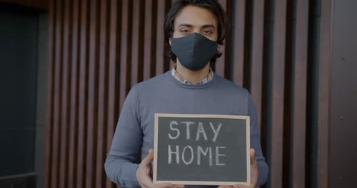 Young Adult Holds Stay Home Sign in Urban Setting