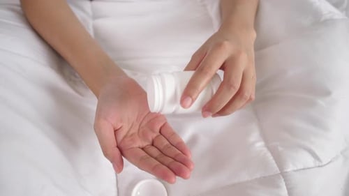 Patient hält Tabletten in der Hand auf dem Bett
