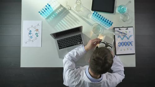 Researcher Writing Observations on Laptop, Viewing Sample Under Microscope