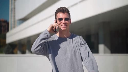 Handsome Caucasian Man with in Sunglasses Walks and Speaks on a Mobile Phone in a City Park