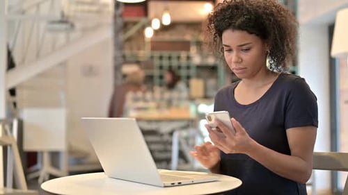 Young African Woman Using Laptop and Smartphone in Cafe