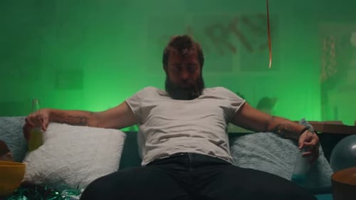 Bearded Man Sits After Party in Messy Living Room