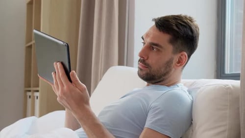 Man Relaxing in Bed Using a Tablet