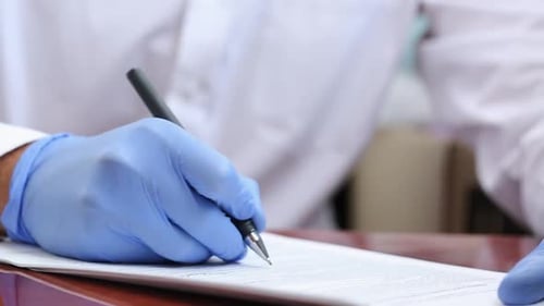 A Doctor in Rubber Gloves Fills Out Documents With a pen. The doctor works with documents