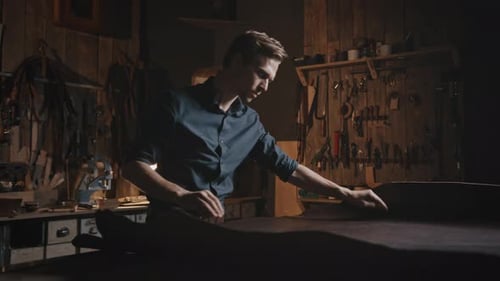 Junge professionelle Wäscherin, die ein Stück echtes Leder ausrollt, untersucht es in der Werkstatt, bevor