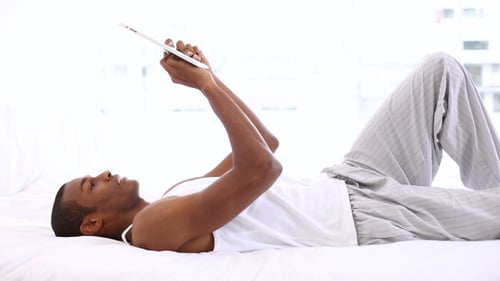 Man Relaxing on Bed with Tablet in Bedroom
