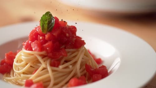 Die Kamera folgt dem Mahlen von Pfeffer über Spaghetti mit frischer Tomatensauce in der Platte. Zeitlupe.