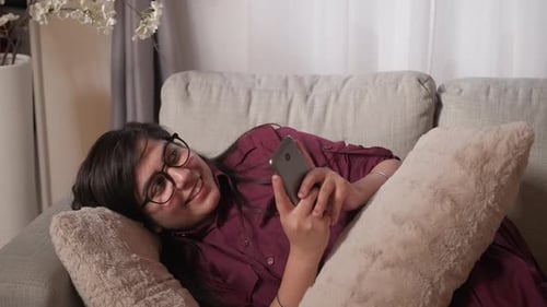 Woman Relaxes on Couch Using Smartphone