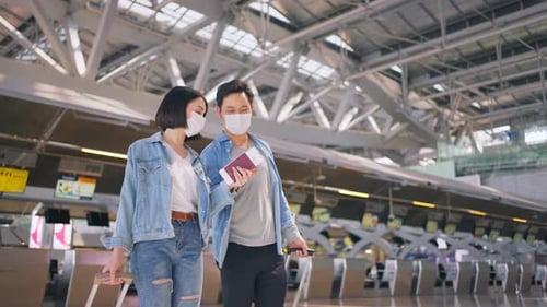 Man and woman passengers wear face mask walking in airport terminal to boarding gate during Covid19.