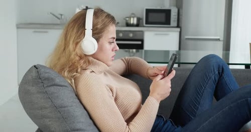 Woman Lounging on Couch with Phone and Headphones