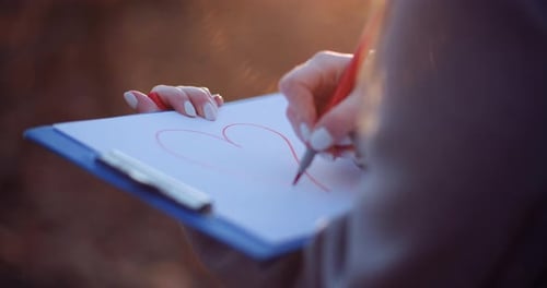 Hand Draws Heart with Red Marker Outdoors