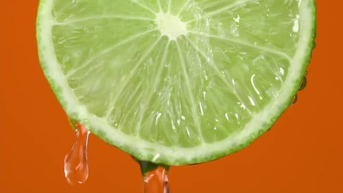 Water drops falling from green hue lime on orange background. Lime slice and water splashing