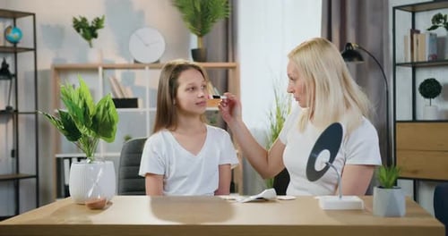 Mère assise à leur table avec sa fille adolescente et lui apprend à se maquiller